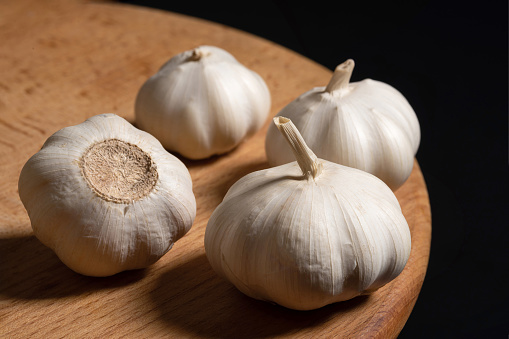 Garlic bulbs on a wooden board black background. Organic garlic, close up.