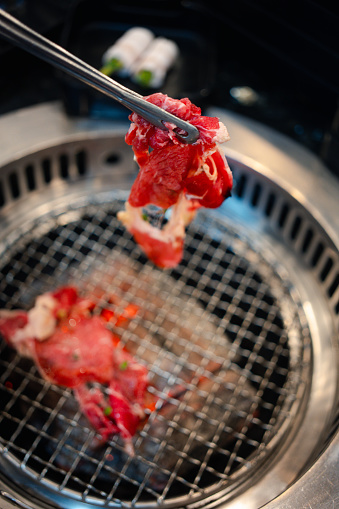 Cropped shot of man having traditional Japanese style beef barbecue Yakiniku in a restaurant and putting raw beef slices over the charcoal grill stove