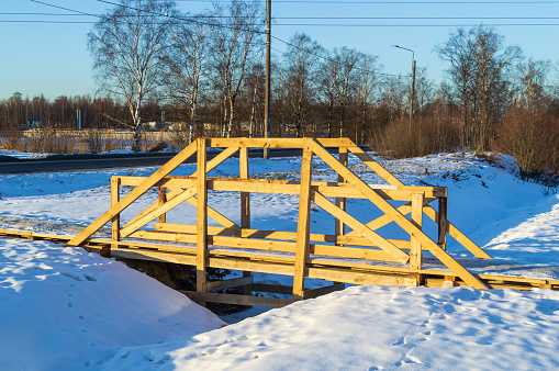 A wooden bridge over a small stream in the snow. The bridge is wooden and has a rustic feel to it. The snow is covering the ground, and the bridge is surrounded by trees. The scene is peaceful