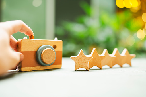 A reviewer is holding a toy camera with 5 wooden star models. Ideas for rating and reviewing products by taking photos for promotional posts.