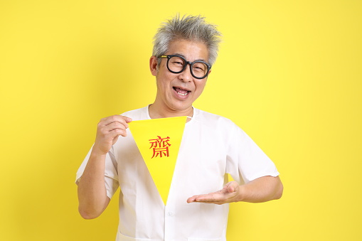 Senior man in white color with gesture of holding Chinese vegetarian festival flag isolated on yellow background. J festival,  Translation for Chinese and Thai text is refrain eating meat or symbol of vegetarian festival.