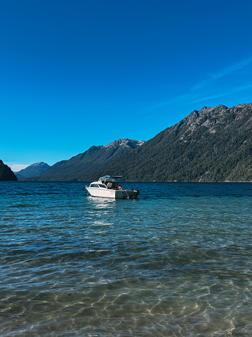 A small boat is floating in the water near a mountain. The sky is clear and blue, and the water is calm. The scene is peaceful and serene, with the boat being the only object in the water
