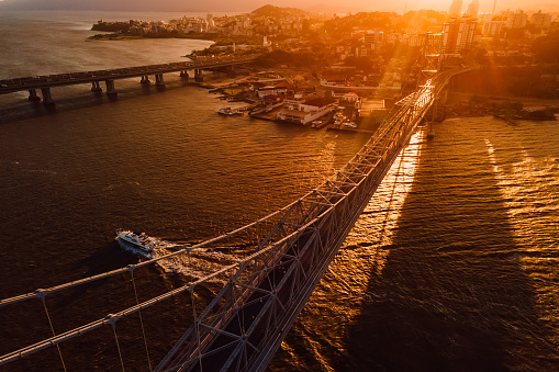Old cable bridge with sunset light and touristic boat in Florianopolis, Brazil. Aerial view