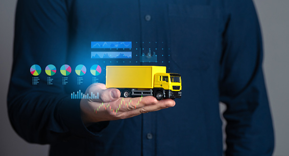 Businessman holding a truck and economic charts. Logistics industry. Transport optimization. Selection of delivery methods, effective number of vehicles and crews.