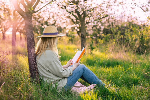 istock Relaxed woman is sitting under blooming cherry tree and reading book to improve her mindfulness 2149010121