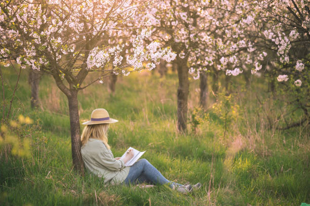 Relaxed woman is writing her diary and resting in blooming cherry orchard