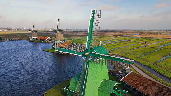 Aerial view of from traditional windmills at Zaanse Schans in the Netherlands, Rotating mills aerial shooting, Rural scene with windmills in Netherlands, Ancient wooden windmills of Zaanse Schans, The most popular tourist destination in the Netherlands\n\nZaanse Schans is a neighbourhood of Zaandam, near Zaandijk, Netherlands. It is best known for its collection of windmills and wooden houses that were relocated here from the wider region north of Amsterdam for preservation. From 1961 to 1974, old buildings from all over the region known as the Zaanstreek were relocated using lowboy trailers to the Zaanse Schans. Two of the windmills in the Zaanse Schans are preserved in their original site where they were first constructed, and therefore don't make up part of the relocated structures. The Zaans Museum, established in 1994, near the first Zaanse Schans windmill, is located south of the neighbourhood. This architectural reserve for Zaanse timber construction is a protected village scene because of its architectural-historical and landscape value. It developed into an international tourist destination with several million visitors every year: in 2016, there were 1.8 million, in 2017 – 2.2 million.
