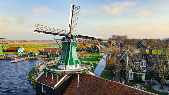 Aerial view of from traditional windmills at Zaanse Schans in the Netherlands, Rotating mills aerial shooting, Rural scene with windmills in Netherlands, Ancient wooden windmills of Zaanse Schans, The most popular tourist destination in the Netherlands\n\nZaanse Schans is a neighbourhood of Zaandam, near Zaandijk, Netherlands. It is best known for its collection of windmills and wooden houses that were relocated here from the wider region north of Amsterdam for preservation. From 1961 to 1974, old buildings from all over the region known as the Zaanstreek were relocated using lowboy trailers to the Zaanse Schans. Two of the windmills in the Zaanse Schans are preserved in their original site where they were first constructed, and therefore don't make up part of the relocated structures. The Zaans Museum, established in 1994, near the first Zaanse Schans windmill, is located south of the neighbourhood. This architectural reserve for Zaanse timber construction is a protected village scene because of its architectural-historical and landscape value. It developed into an international tourist destination with several million visitors every year: in 2016, there were 1.8 million, in 2017 – 2.2 million.