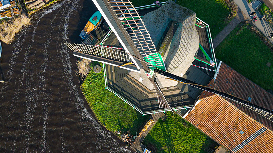 Aerial view of from traditional windmills at Zaanse Schans in the Netherlands, Rotating mills aerial shooting, Rural scene with windmills in Netherlands, Ancient wooden windmills of Zaanse Schans, The most popular tourist destination in the Netherlands

Zaanse Schans is a neighbourhood of Zaandam, near Zaandijk, Netherlands. It is best known for its collection of windmills and wooden houses that were relocated here from the wider region north of Amsterdam for preservation. From 1961 to 1974, old buildings from all over the region known as the Zaanstreek were relocated using lowboy trailers to the Zaanse Schans. Two of the windmills in the Zaanse Schans are preserved in their original site where they were first constructed, and therefore don't make up part of the relocated structures. The Zaans Museum, established in 1994, near the first Zaanse Schans windmill, is located south of the neighbourhood. This architectural reserve for Zaanse timber construction is a protected village scene because of its architectural-historical and landscape value. It developed into an international tourist destination with several million visitors every year: in 2016, there were 1.8 million, in 2017 – 2.2 million.