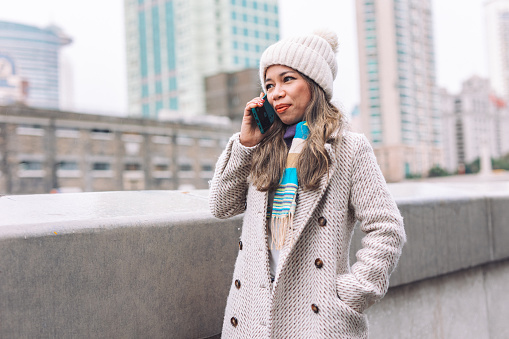 Woman talking on her mobile phone. She is dressed warmly in a knit cap and jacket, indicating a chilly day outdoors in city.