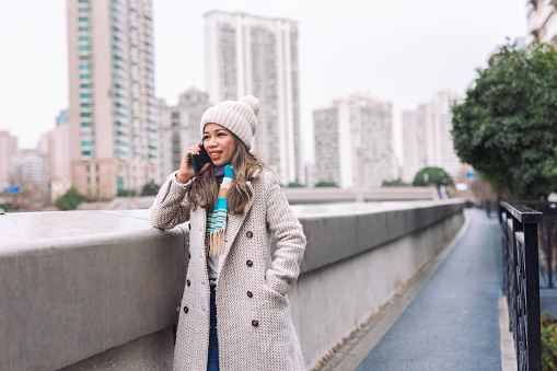 Woman talking on her mobile phone. She is dressed warmly in a knit cap and jacket, indicating a chilly day outdoors in city.