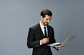 Man business stares at laptop and works thoughtfully online smiling over the internet in business suit video call business talks on gray background copy place