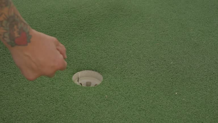 tattooed hand gets golf ball out of hole