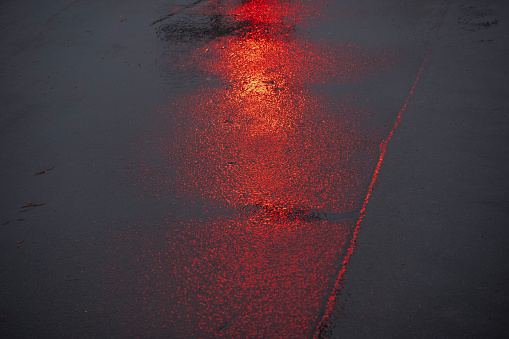 reflections of a red traffic light on wet asphalt in rainy weather in the evening