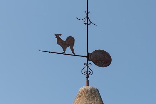 Rusty rooster weather vane on the rooftop on a sunny day.