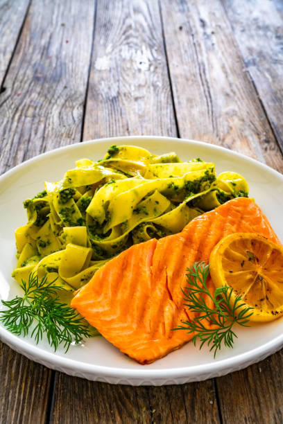 Pappardelle with grilled salmon steak and basil pesto on wooden table