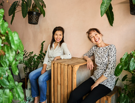 Portrait of two senior asian female friends sitting at cafe table looking at camera and smiling