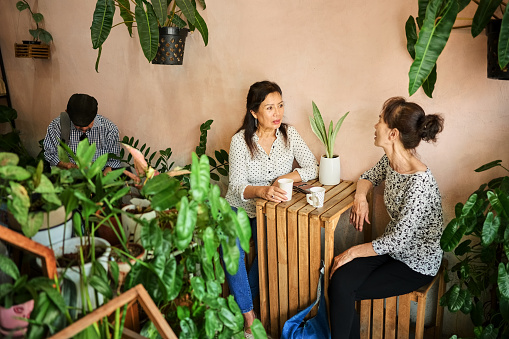 Senior Asian woman talking with her friend while sitting together at small wooden table in street cafe