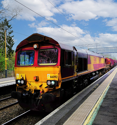 April 18th. 2024. A diesel freightliner locomotive is pulling a goods / freight train with containers at Barnt Green Station West <idlamds, England UK. It is a sunny day in Spring and there are no visible people in the picture.