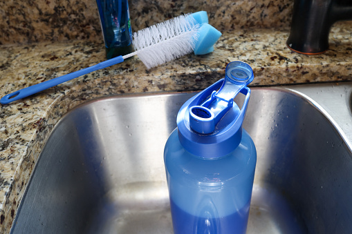 Cleaning a dirty reusable plastic water bottle in a kitchen sink