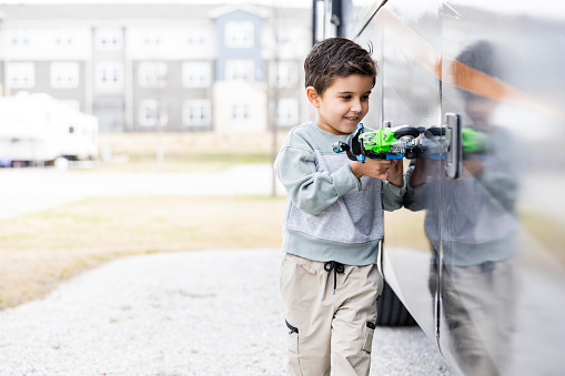 While taking a break from traveling, the preschool aged boy plays with his toys outside the RV.