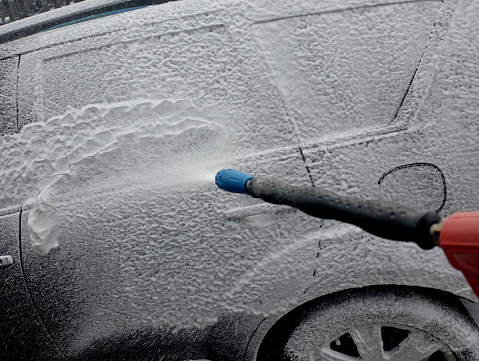 From a special gun at the car wash, white foam is applied to the car for chemical cleaning of the vehicle surface.
