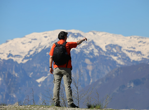 Young male hiker pointing at snowcapped mountains with backpack on during high altitude hike