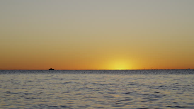 Silhouette Of A Boat Sitting at the Horizon Against A Colorful Orange Sunset Sky Over Seascape. Wide Shot