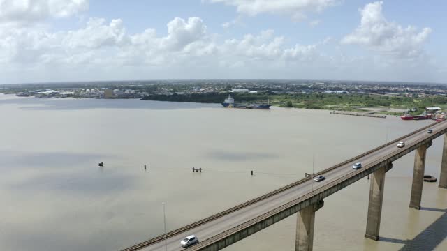 Wide angle aerial shot of Jules Wijdenbosch Bridge between Paramaribo and Meerzorg in Suriname, South America, with heavy traffic as drone gains backwards, revealing bridge