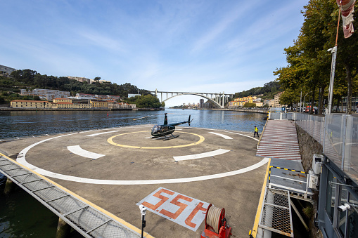 Porto Portugal - 5 September 2023 - Heliport on the Douro River in Porto with a Robinson R44 helicopter preparing for flight - the Ponte da Arrabida bridge in the background