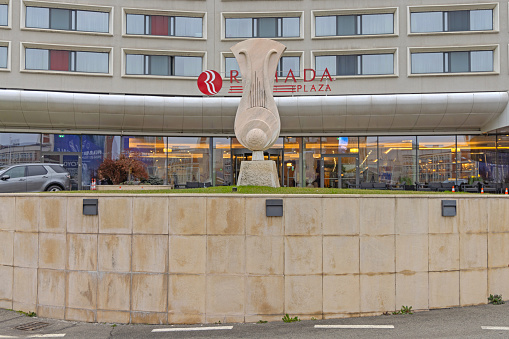 Craiova, Romania - March 15, 2024: Stone Sculpture in Front of Four Star Ramada Plaza Hotel by Wyndham Building at Bucharest Road.