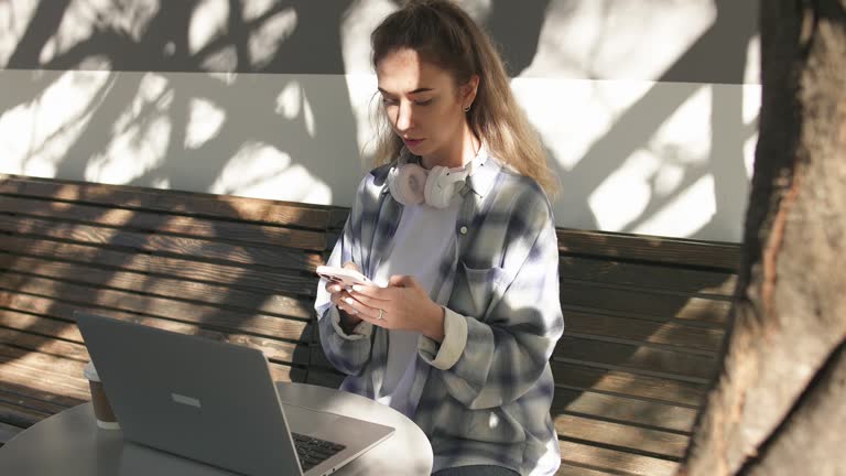 Young woman in plaid shirt spending lunch break in cafe surfing internet on smartphone