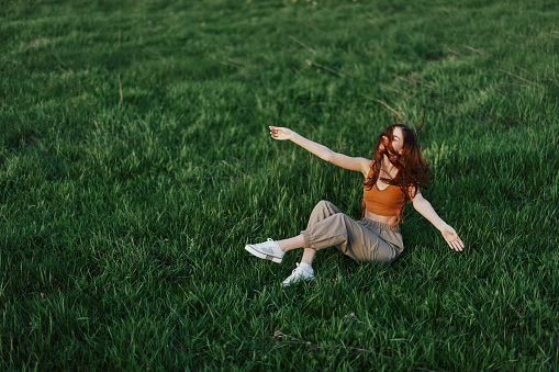 Young woman playing games in the park on the green grass spreading her arms and legs in different directions falling and smiling in the sunlight of summer, a lifestyle of life and youth. High quality photo