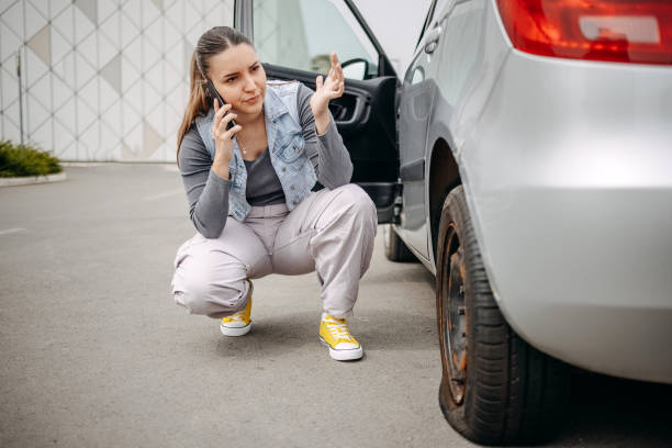 istock Woman looking at flat tyre on her car and asking for help using mobile phone 2149025370