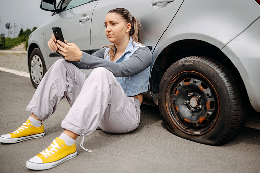 Young beautiful asking for help using smart phone having a flat tyre on her vehicle