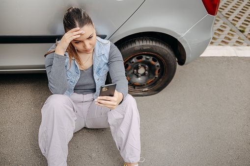 Young beautiful woman using smart phone to ask for assistance on the road because of flat tyre