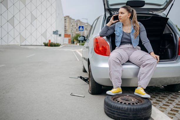 istock Woman sitting on back of her car asking for support using mobile phone because having a flat tyre 2149025495
