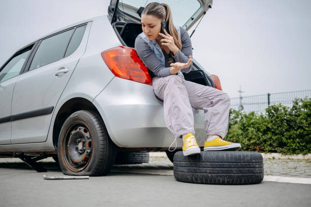 istock Woman sitting on back of her car asking for support using mobile phone because having a flat tyre 2149025527