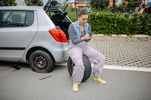 Young beautiful woman using smart phone asking for help having a flat tyre on the road