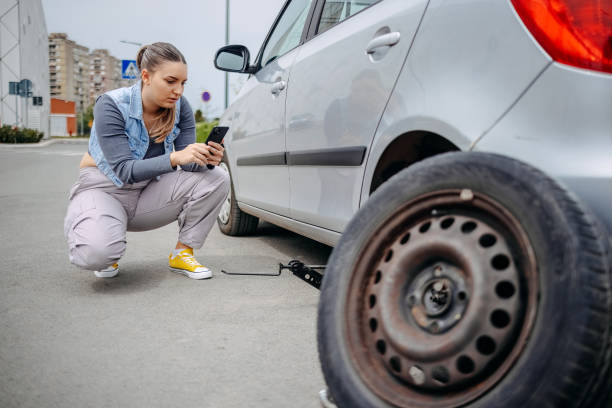 istock Woman changing flat tyre on her car and using mobile phone to ask for assistance 2149025554