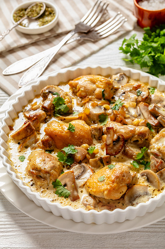 chicken thighs in a creamy mushroom garlic sauce with herbs and parmesan cheese in white baking dish on white wooden table with forks, vertical view from above, close-up