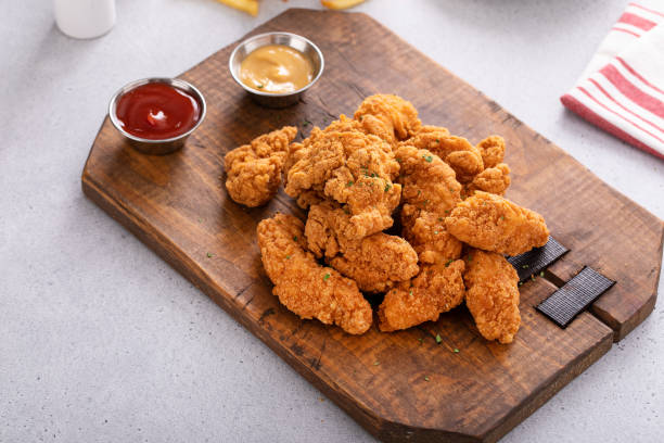 istock Chicken nuggets or chicken strips on a board with dipping sauces, fries and celery 2149028280
