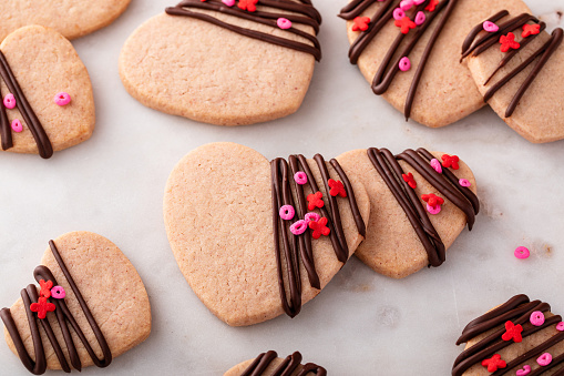 Heart shaped cookies with strawberry flavor, drizzled with dark chocolate with pink sprinkles on a serving board
