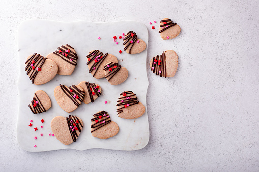 Heart shaped cookies with strawberry flavor, drizzled with dark chocolate with pink sprinkles on a serving board