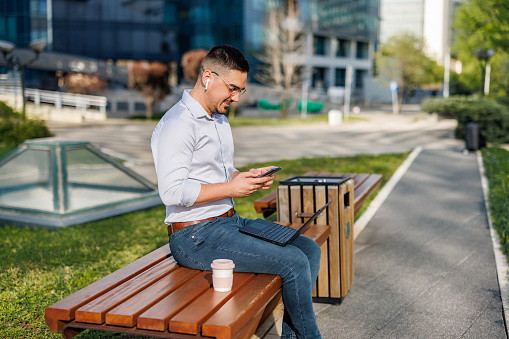 Taking productive pauses on a city bench, a mid-adult businessman uses his laptop to catch up on work, proving that effective time management often includes changing up the scenery
