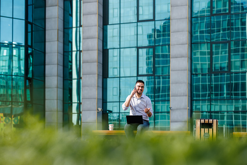 Innovating his work routine, a mid-adult businessman finds solace and focus on a bench, where he can tackle his workload with a fresh perspective, energized by the city's dynamic atmosphere