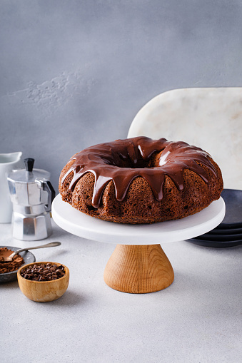 Chocolate bundt cake with chocolate ganache on top on a cake stand on white table