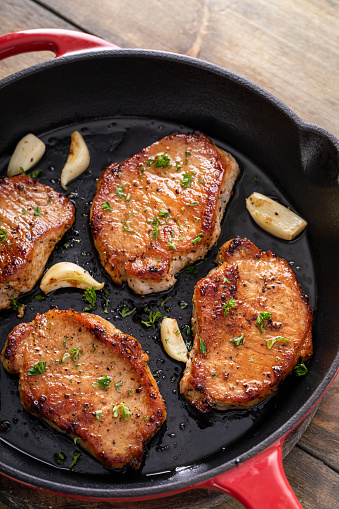 Pork chops seared in a cast iron pan with garlic and herbs