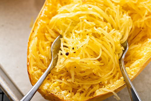 Spaghetti squash baked and pulled apart with two forks, ready to eat on a baking pan