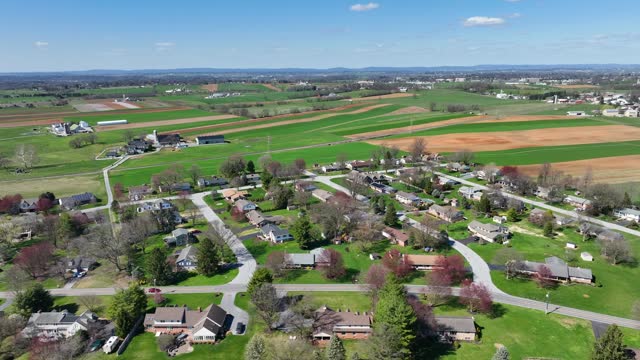 Small American suburb and farm house with rural fields during sunlight in spring. Quiet Neighborhood in suburbia of Pennsylvania. Idyllic drone scene. Aerial lateral wide shot.